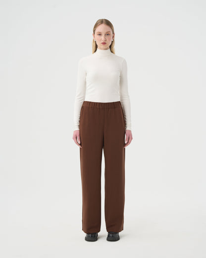 Chandail Turtleneck blanc ivoire pour femme et pantalon ample brun à taille élastique. 